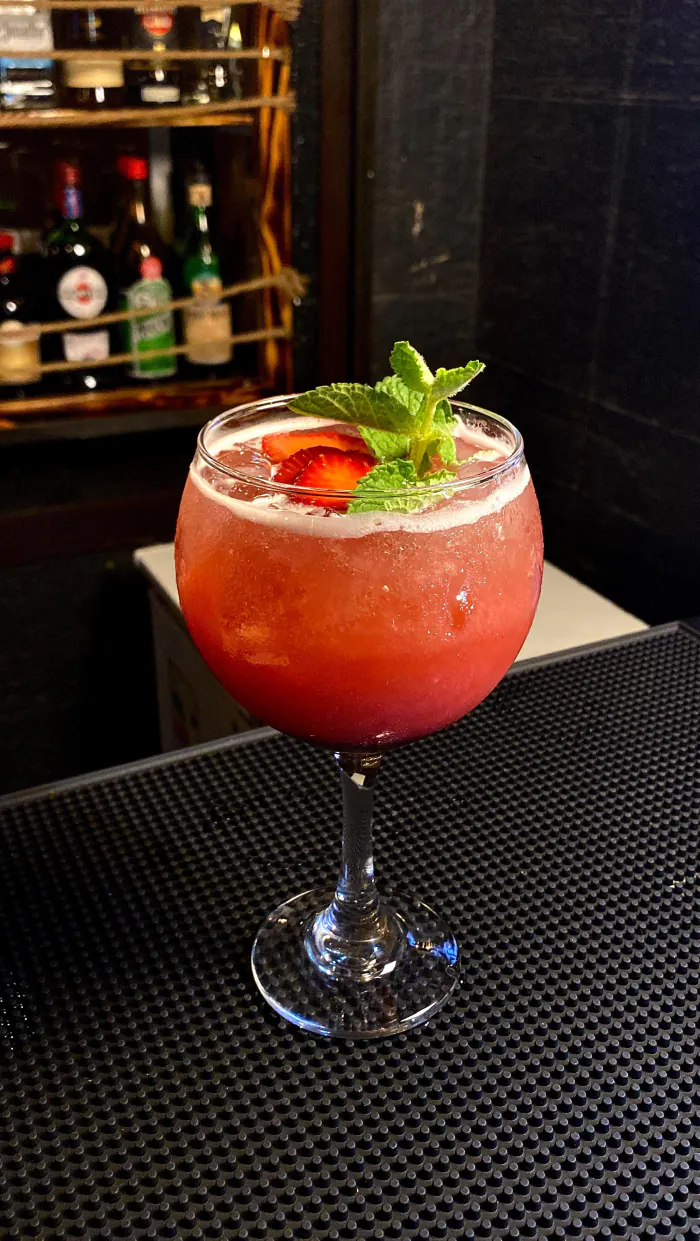 Cóctel de frutilla con menta sobre la barra, con botellas al fondo